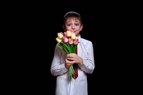 Mignon garçon en chemise blanche avec un bouquet de tulipes. Isoler sur fond noir — Photo