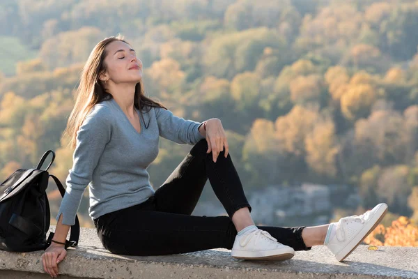 Beautiful girl enjoys nature sitting on a hill with closed eyes. Sunny day