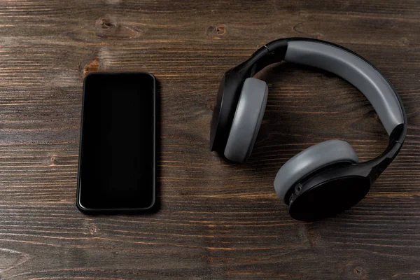Hörlurar och telefon på en mörk trä bakgrund. Den moderna mannens prylar. — Stockfoto