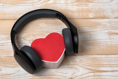 Tam boyutlu kablosuz kulaklıklar açık kahverengi tahta bir masada kırmızı kalp şeklinde küçük bir kutuyu kenara çekti. Müzik konseptini seviyorum