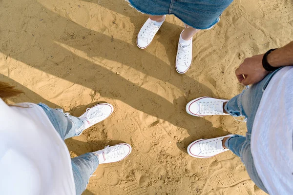 Shoes selfie from above. Teenagers stand on sand in white sneakers. Top view