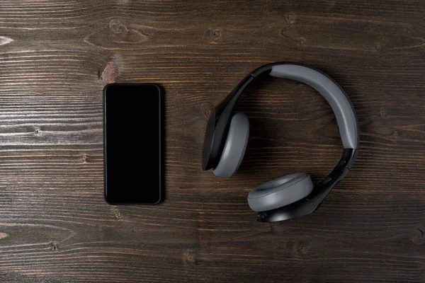 Smartphone y auriculares sobre un fondo de madera oscura. El secado de la música. Vista superior —  Fotos de Stock