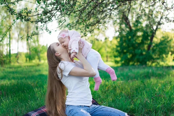 Happy smiling young mother holding little baby daughter over nature background. Child and parenthood concept — Stock Photo, Image