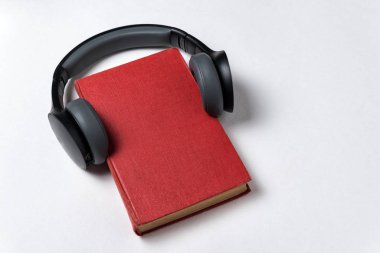 Beyaz arka planda kulaklıkları olan kırmızı defter. Sesli kitap konseptiyle öğreniyorum. Boşluğu kopyala