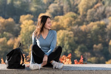 Kız doğanın arka planında oturuyor ve gülümsüyor. Bağımsız seyahat