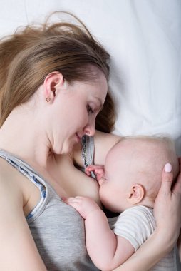 Yatağında tatlı bir bebekle yatan bir anne. Emzirme. Mutlu aile konsepti Top view