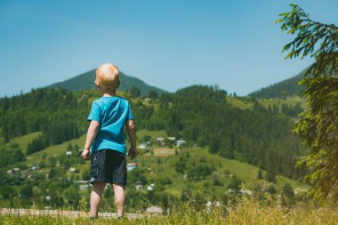 Dağların arkasında duran sarı saçlı çocuk. Çocuklarla seyahat etmek. Arka plan