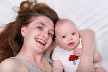 Genç anne 3 aylık kızına sarılıyor. Gülümseyen anne ve çocuğun portresi.