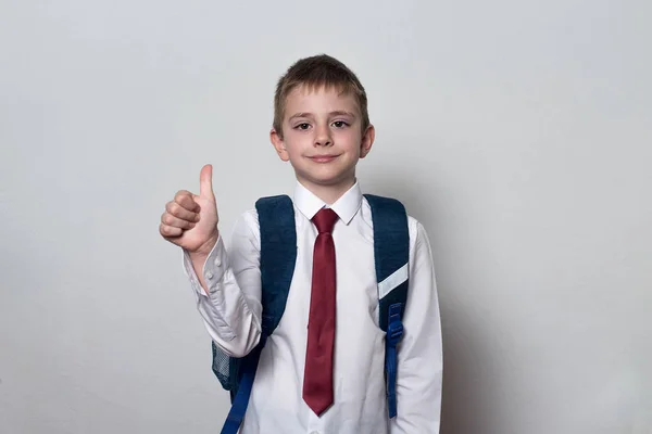 El chico con uniforme escolar muestra los pulgares hacia arriba. Fondo blanco. Educación infantil . —  Fotos de Stock