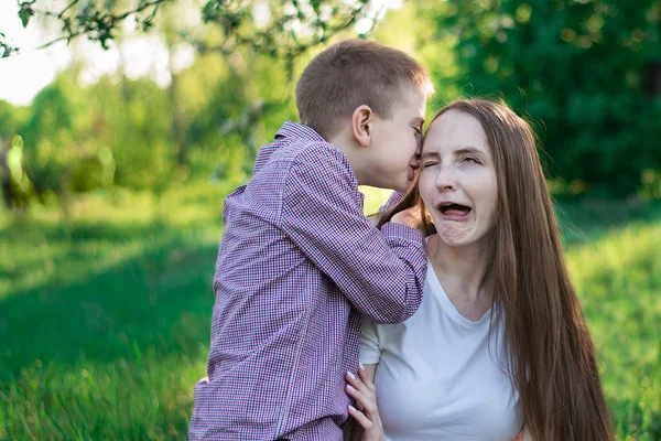 Jonge moeder heeft plezier met zoon. Positieve moeder met kind in het park. Gekke gezichtsuitdrukking. — Stockfoto