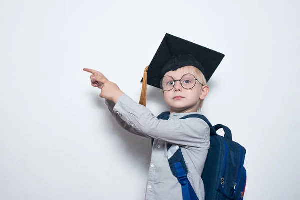 Garçon blond en lunettes avec un look sérieux montre à bord. Garçon portant un chapeau étudiant. Réalisation des enfants. Espace de copie — Photo