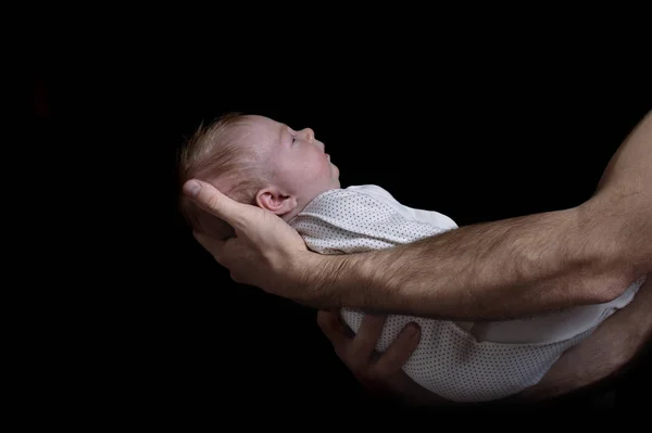 Manliga händer som håller i ett barn. Spädbarn sover. Svart bakgrund. Sidovy, isolerad — Stockfoto