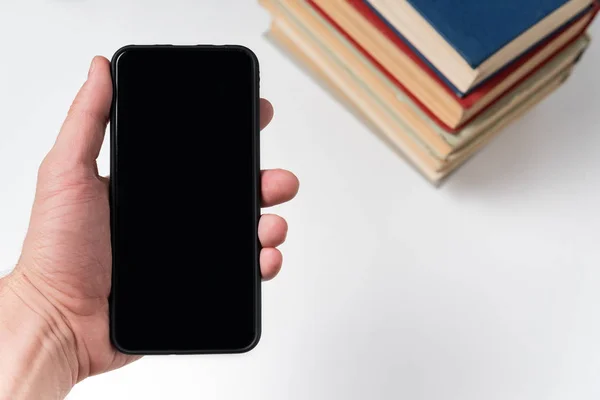 Mobile phone in hand on the background of books. E-book concept. White background, copy space — Stock Photo, Image