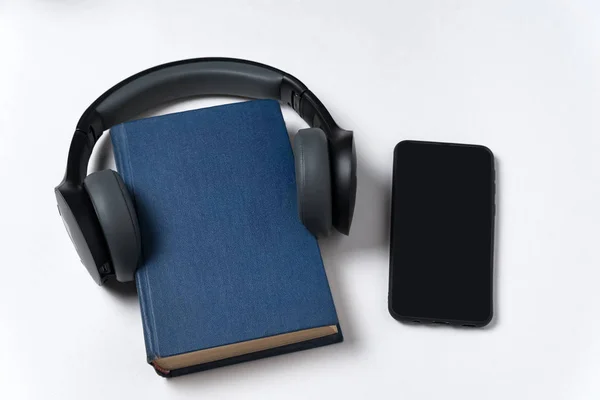 Book, headphones and smartphone on white background. Listen to books on your phone. Audiobook concept. — Stock Photo, Image