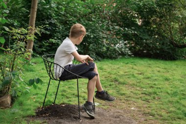Genç bir çocuk doğanın arka planında tek başına oturuyor. Park 'ta kal. yan görünüm