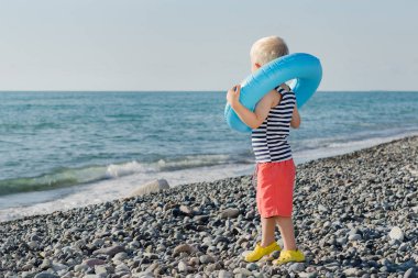Şirin sarışın çocuk şişme yüzük takmış ve denize bakıyor. Güvenli yüzme konsepti