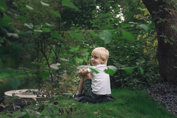 Маленький блондин, сидящий на траве в парке. Независимый ребенок — стоковое фото