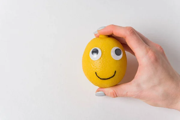 Legrační citron s očima a úsměvem na bílém pozadí. Ženská ruka držící citrónový úsměv — Stock fotografie