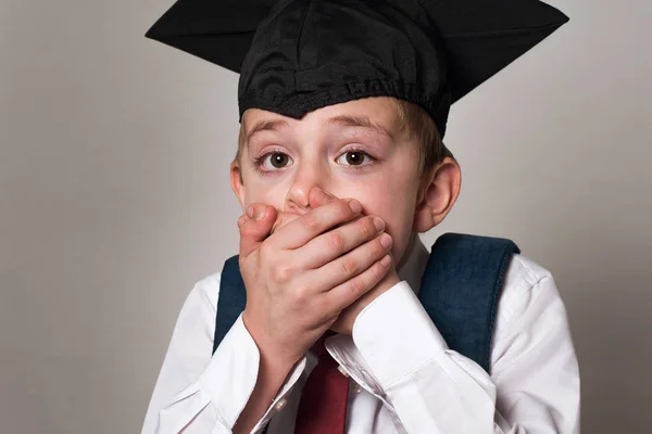 Startled schoolboy covered his mouth with hands. Boy in student hat. White background. Middle School. — Stock Photo, Image