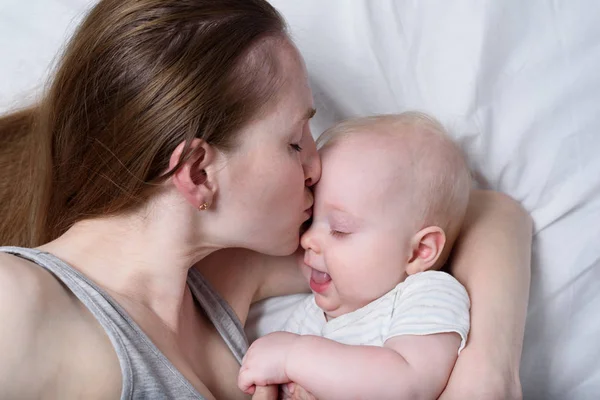 Joyeux maman tenant bébé sur les mains. Belle jeune mère embrassant son bébé . — Photo