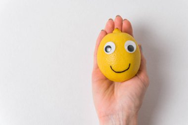 Komik limon meyvesi karakteri beyaz arka planda bir kadının elinde yatıyor. Neşeli meyveler, gözler ve gülümseme..