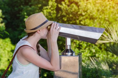 Genç kadın, Park arka planında turistler için dürbünden bakıyor.