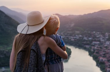 Arka planda, genç oğlunu kucaklayan anne manzarası. Çocuk konseptiyle seyahat.