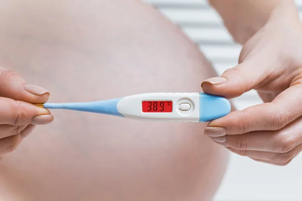 Pregnant woman with a electronic thermometer. high temperature, disease during pregnancy concept.