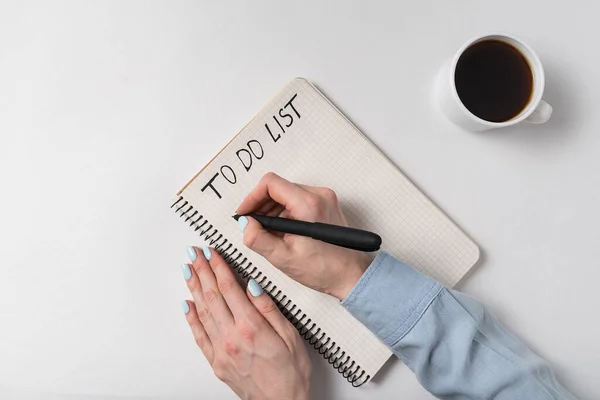 リストを作るために メモ帳に女性の手を書く 白を基調としたノートとコーヒーカップ手書き — ストック写真