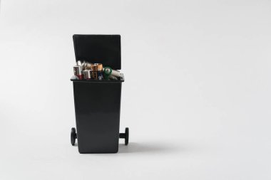 Beyaz arka plandaki çöp konteynırında kullanılmış piller. Zehirli ev atıklarıyla çevre kirliliği.