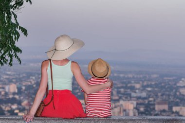 Genç anne ve oğul şehrin manzarasına tepeden bakıyor. Kadın oğluna sarılıyor. Arka plan.