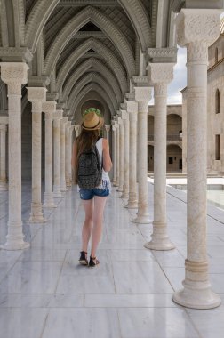 Genç bir kadın kadim galeride sütunlarla yürüyor. Antika sütunlar.