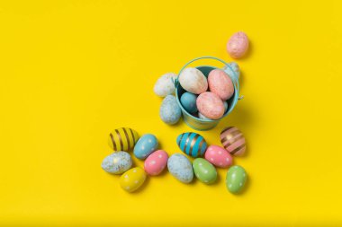 Parlak sarı arka planda renkli Paskalya yumurtaları olan kova. Bir sürü renkli yumurta..