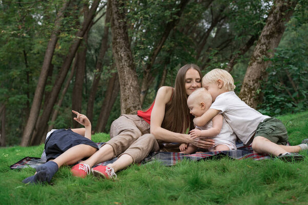 Family picnic at gaden park outdoors. Mom and three children rest on picnic blanket