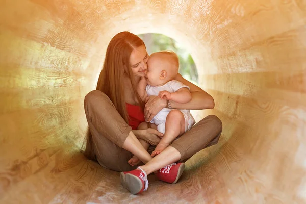 Young mother and happy baby playing in wooden tunnel. Eco-friendly natural playground.