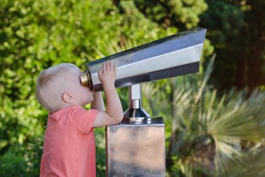 Küçük çocuk, turistler için dürbünle Park arka planına bakıyor..