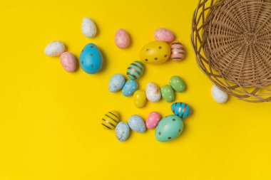 Sarı arka planda sepetin yanında bir sürü renkli Paskalya yumurtası var. Neşeli yumurtaların en üst görüntüsü.