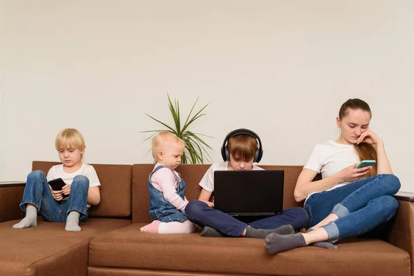 母及び3人の子供はソファに坐り 電話およびラップトップを使用する 人々と技術の中毒 — ストック写真