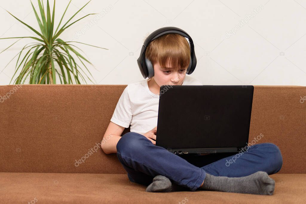 Boy teenager sitting on couch with laptop in hand and stereo headphones. computer games addiction concept.