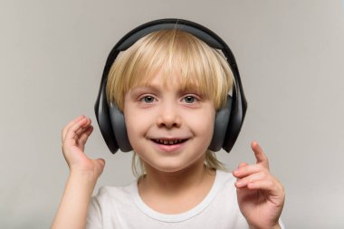 Hafif arka planda kulaklıklı sarışın çocuk. Çocuk müzik dinler ve gülümser..