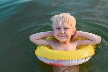 Şişme lastik çemberli mutlu küçük çocuk suyun üzerinde eğleniyor. Lastik halkalı çocuk