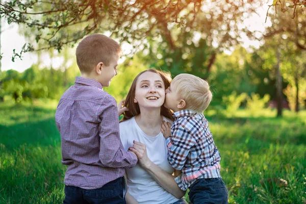 Mom with two sons in the Park. Child is kissing his mother. Happy motherhood.