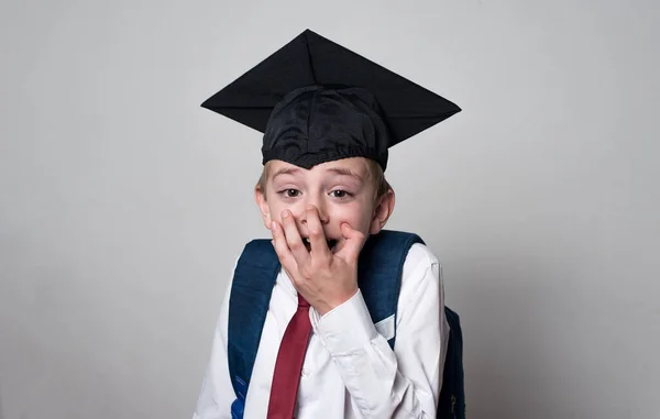 Surprised student covered his mouth with his hands. Boy wearing graduate hat. Junior high school concept.