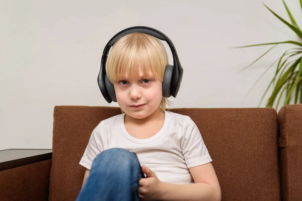 ソファに座ってヘッドフォンで公正な髪の男の子 十代の若者は音楽を聞く — ストック写真