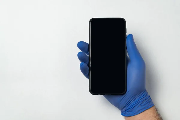 Beyaz arka planda akıllı telefon tutan mavi nitrile eldivenlerini teslim et. Boş siyah ekran. Uzayı kopyala Model.