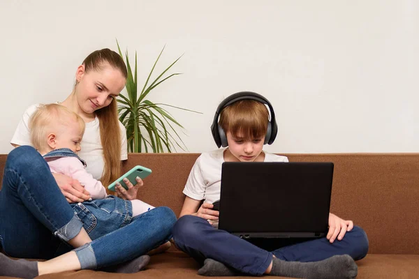 赤ちゃんを持つ若い母親は次座っているモバイルの息子であり ノートパソコンを見て ファミリーガジェット中毒 — ストック写真