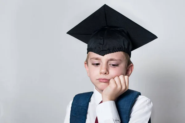 Sad boy in a student hat propped his head with his hand. Failed exam. Portrait on a white background
