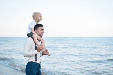 Küçük çocuk babasının omuzlarında oturuyor. Genç yakışıklı adam ve oğlu. Büyük ve küçük kardeşler.