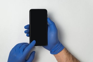 Mavi eldivenli eller beyaz arka planda akıllı telefon tutuyor. Boş ekran. Uzayı kopyala Model.