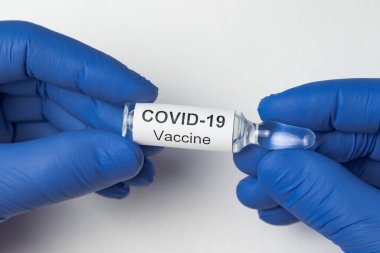 Mikrobiyolog beyaz arka planda Covid-19 etiketli ampul tutuyor. Koronavirüs aşısı..